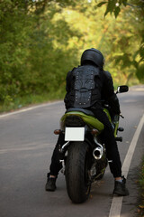 Fototapeta premium motorcyclist in black protective suit and helmet near green sports motorcycle