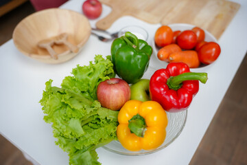 Fresh lettuce, peppers, and apples are being prepared for a salad on a white kitchen table
