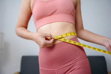Focused on health, a woman measures her waist at home, tracking fitness progress with determination...