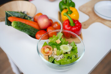 Glass bowl filled with a chicken salad surrounded by fresh ingredients on a white table