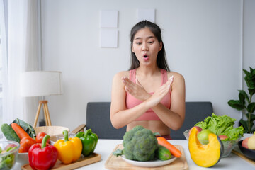 Young woman is showing a stop sign with her hands in front of a table full of healthy food,...
