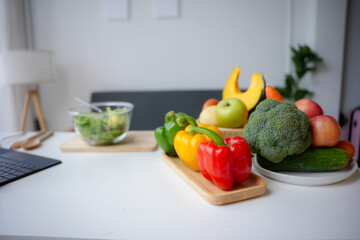 White table full of fresh vegetables and fruits with a laptop lying on it, suggesting a healthy lifestyle