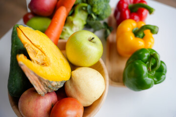 Variety of colorful fresh organic vegetables and fruits are arranged on a white table, promoting a healthy lifestyle