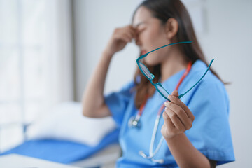 Young nurse having a moment of respite in a hospital room, massaging her eyes and holding her...