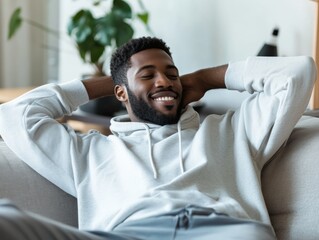 Obraz premium A relaxed young man enjoys a moment of leisure, sitting comfortably on a couch in a bright, modern living space.