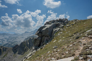 Fracturing rocks hang over steep cliffs in Southern Pirin Mountains in Bulgaria, July shot during partly cloudy weather with beautiful cumulus clouds.