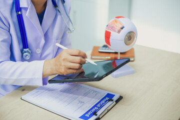 An ophthalmologist explains eye diseases using an eye model at an examination table in a hospital examination room. Glaucoma, cataracts, diabetic retinopathy.