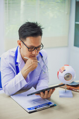 An ophthalmologist explains eye diseases using an eye model at an examination table in a hospital...