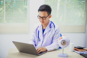 An ophthalmologist explains eye diseases using an eye model at an examination table in a hospital...