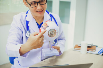 An ophthalmologist explains eye diseases using an eye model at an examination table in a hospital...