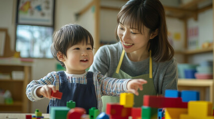 保育園でエプロンをつけた女性の保育士と幼児の保育園児が笑顔でカラフルな積み木で遊んでいる