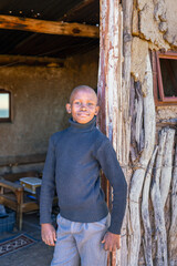 african village, proud boy standing in front of his room, mud hut in the background, door entrance