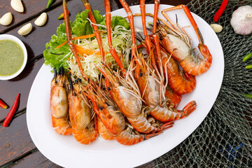 Lots of grilled river prawns are placed in woven containers and sauce bowls are decorated on a wooden background. seafood style