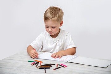 A toddler draws with colored pencils in a sketchbook while sitting at a table in the nursery.