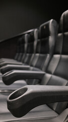 Rows of empty black leather cinema seats with cup holders and numbered backrests in a modern movie...