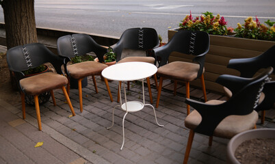 Modern Outdoor Cafe Seating: Stylish Black and Brown Chairs with White Table on Urban Sidewalk