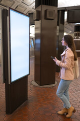 Metro station, a young woman looking at a wall map for directions, holding a cellphone with copy space.