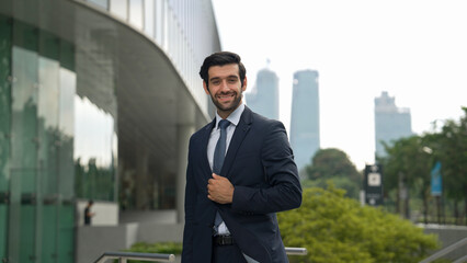 Fototapeta premium Professional businessman standing at city or park. Smiling project manager looking at camera while smiling arms with confident. Closeup of investor wearing suit at architectural building. Exultant.