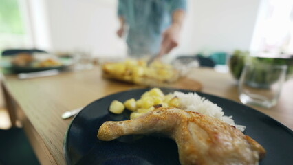 Close-up of a meal featuring chicken, rice, and vegetables with a person serving in the blurred background. home-cooked meals and the joy of serving food to loved ones