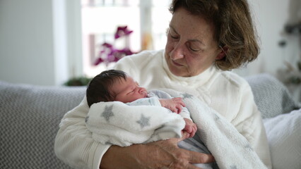 Elderly woman gazing lovingly at newborn baby, heartfelt family moment, intergenerational connection, grandmother and grandchild, cozy living room, nurturing home environment