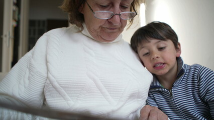 Close-up of an elderly woman's hand pointing at a book page while her grandson attentively follows along, moment of shared learning and intergenerational connection, storytelling