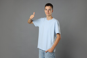 Teenage boy wearing light blue t-shirt and showing thumbs up on grey background