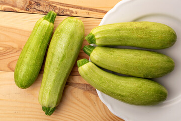 Several ripe zucchini with a ceramic plate on a wooden table, macro, top view.
