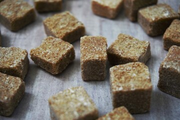 A close-up shot of brown sugar cubes scattered on a wooden surface, highlighting their texture and natural appearance, perfect for sweetening beverages or baking.
