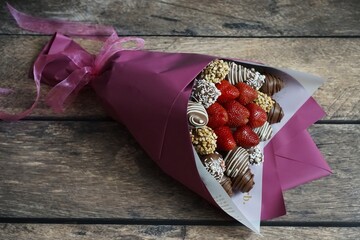 A beautifully wrapped bouquet featuring fresh strawberries and assorted chocolate-covered treats, elegantly arranged in pink wrapping paper, perfect for gifting on special occasions.
