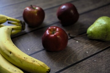 A collection of fresh fruits, including red apples, bananas, and a green pear, arranged on a rustic wooden table, capturing the simplicity of healthy eating.
