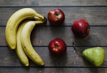 A top-down view of fresh bananas, red apples, and a green pear arranged on a wooden surface, showcasing a simple and natural fruit selection.

