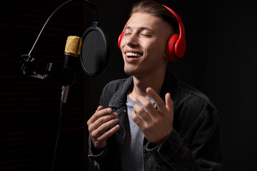 Man wearing headphones singing into microphone in professional record studio