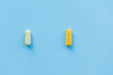 two tablets of different colors yellow and white on a plain blue background, drug or medical addiction, choosing the right and wrong pill