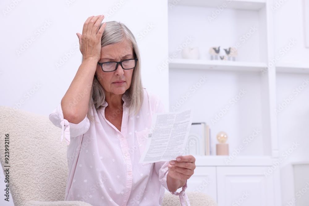 Canvas Prints Senior woman reading medicine instruction in armchair at home