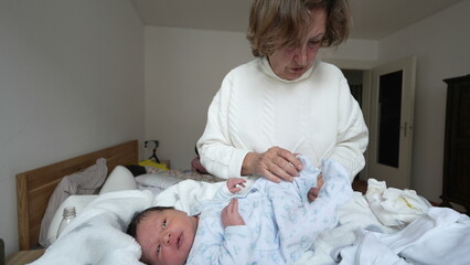 Grandmother cleaning up after changing newborn's diaper. She throws away soiled diapers while the...