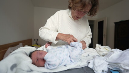Grandmother lovingly dressing newborn in white onesie. baby lies on a soft blanket, mouth open in surprise, capturing a heartwarming moment of generational bonding and tender care in early life