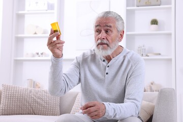 Fototapeta premium Senior man holding bottle with pills at home