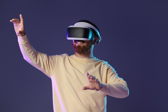 Smiling man using virtual reality headset on dark purple background
