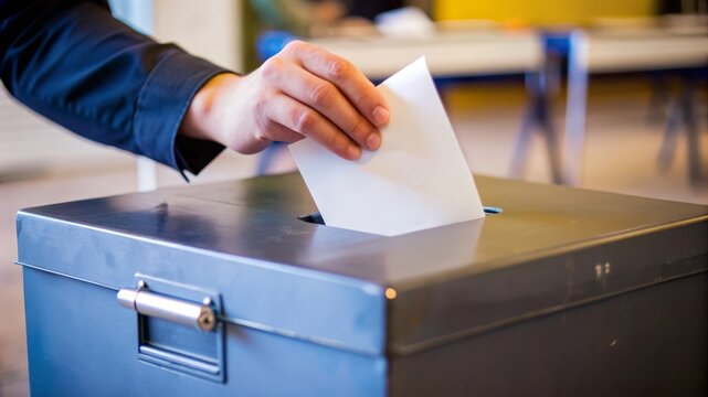 A person's hand carefully places a ballot into a voting box, symbolizing democracy, civic duty, political participation, and the power of the vote.
