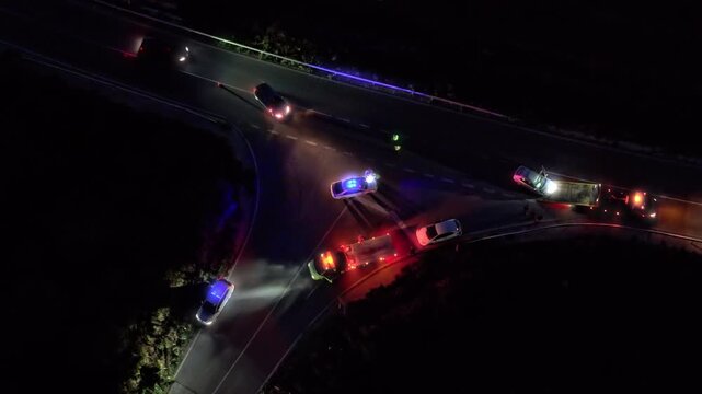 Aerial view of night car accident with involved pedestrian. Roadside assistance loads wrecked car, police direct traffic