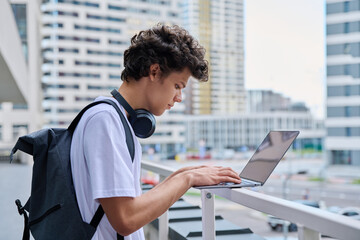 Young handsome male using laptop computer, modern city skyscrapers background