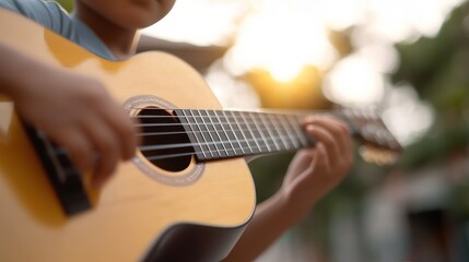 Obraz premium A child enjoys playing acoustic guitar outdoors during sunset, showcasing the joy of music and creativity in a serene environment.