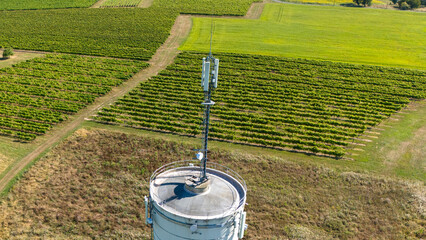 Fototapeta premium Aerial Close-Up of Water Tower with 5G Antenna Overlooking Vineyards and Farmland