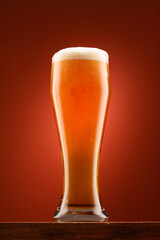 a glass of beer, a wooden stand, a red background, a close-up view of the object, beer bubbles and foam