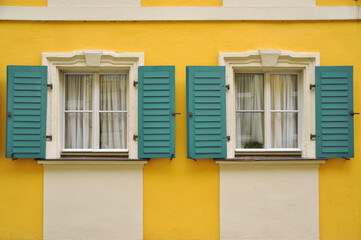 Bright yellow wall with two windows featuring teal shutters