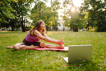 Happy woman practicing Pilates lesson online outdoors. Doing sport following guide or online...