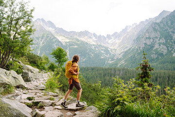 Naklejka premium Smiling female with backpack on hike in nature. Beautiful woman hiker standing on mountain trail and looking at camera smiling. Lifestyle, adventure, nature, active life.