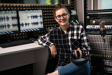 Smiling cute girl sound engineer in a recording studio. Sits among professional equipment and looks...