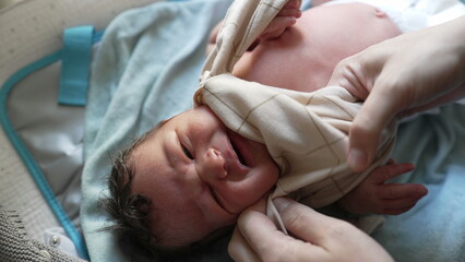 Mother dressing newborn baby, lifting shirt over head, tender moment of care, emphasizing parental love and attention, early stages of infant care, intimate and nurturing scene