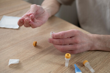 Male fingers closeup, man performing self-administered medical test pricking finger and collecting blood in tube, rapid diagnostic at-home test